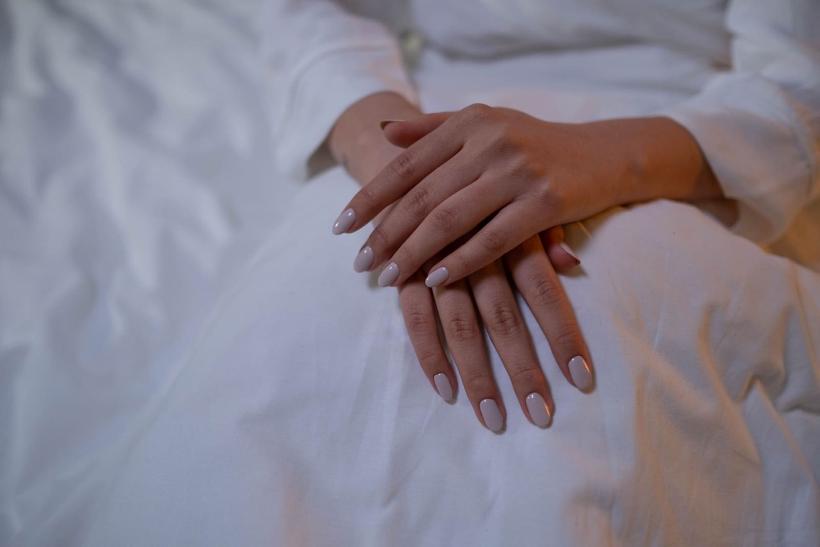 Milky nude manicure, hands resting on white linen